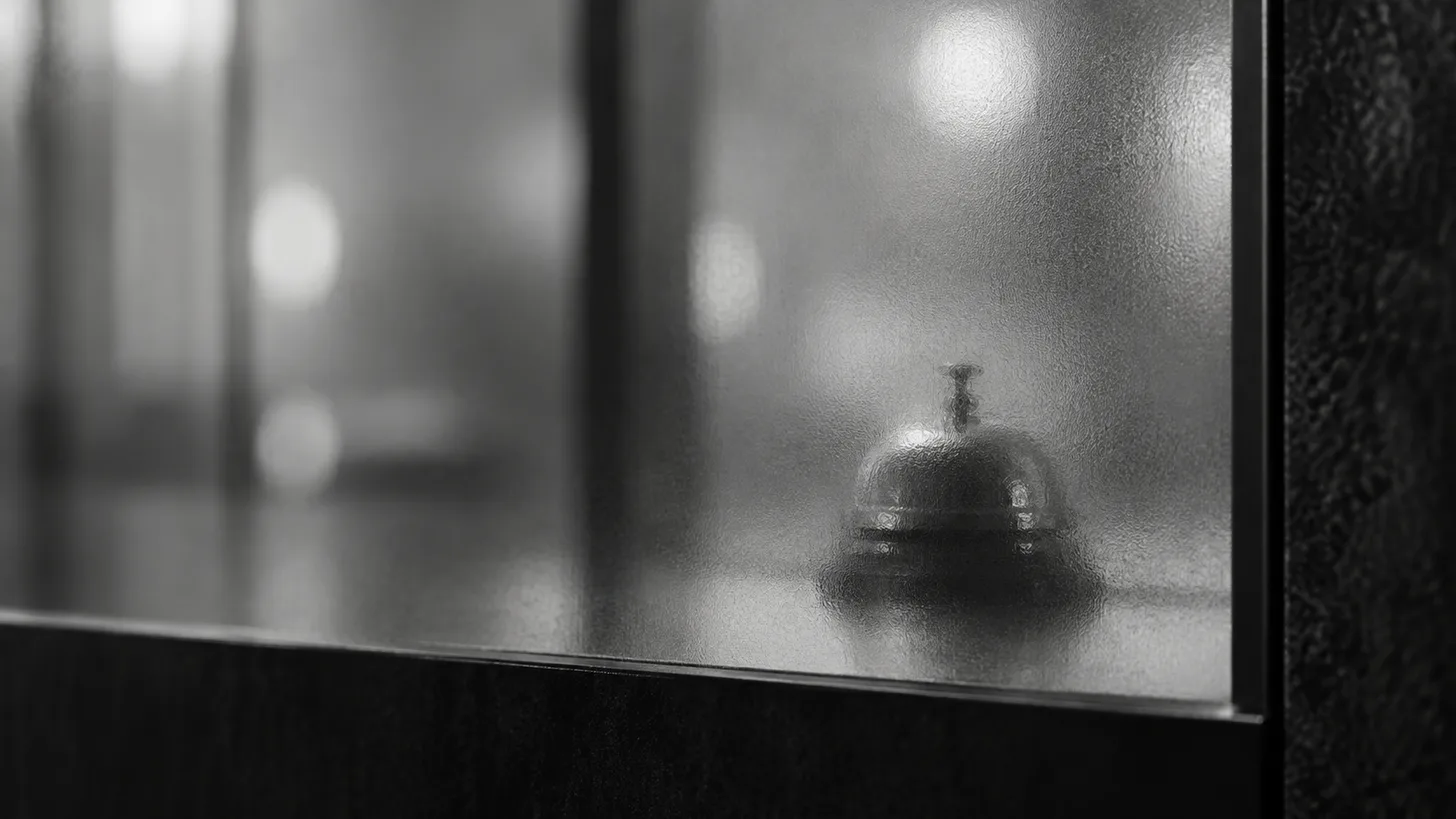 A small physical desk bell behind frosted glass, soft distant round reflections.