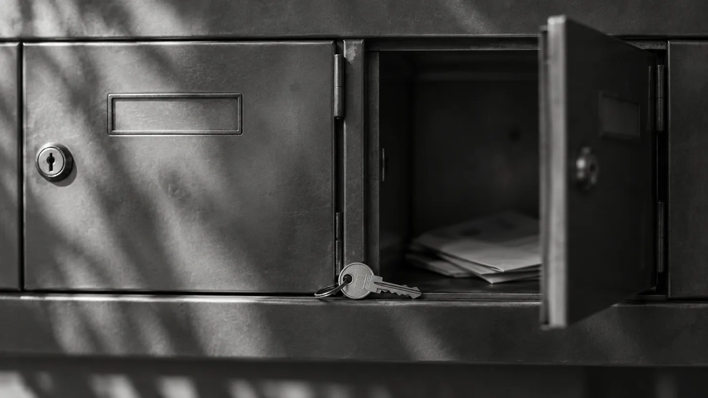 Two adjacent unmarked metal mailbox doors, one open, with a shared key resting between them.