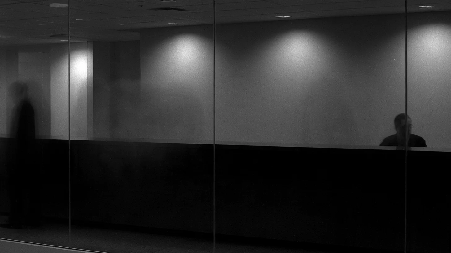 Two indistinct people behind glass at a long office counter.