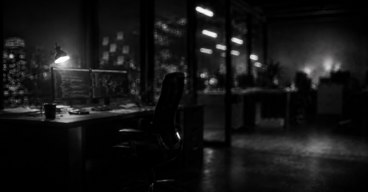 An empty office at night with a desk lamp and monitors.