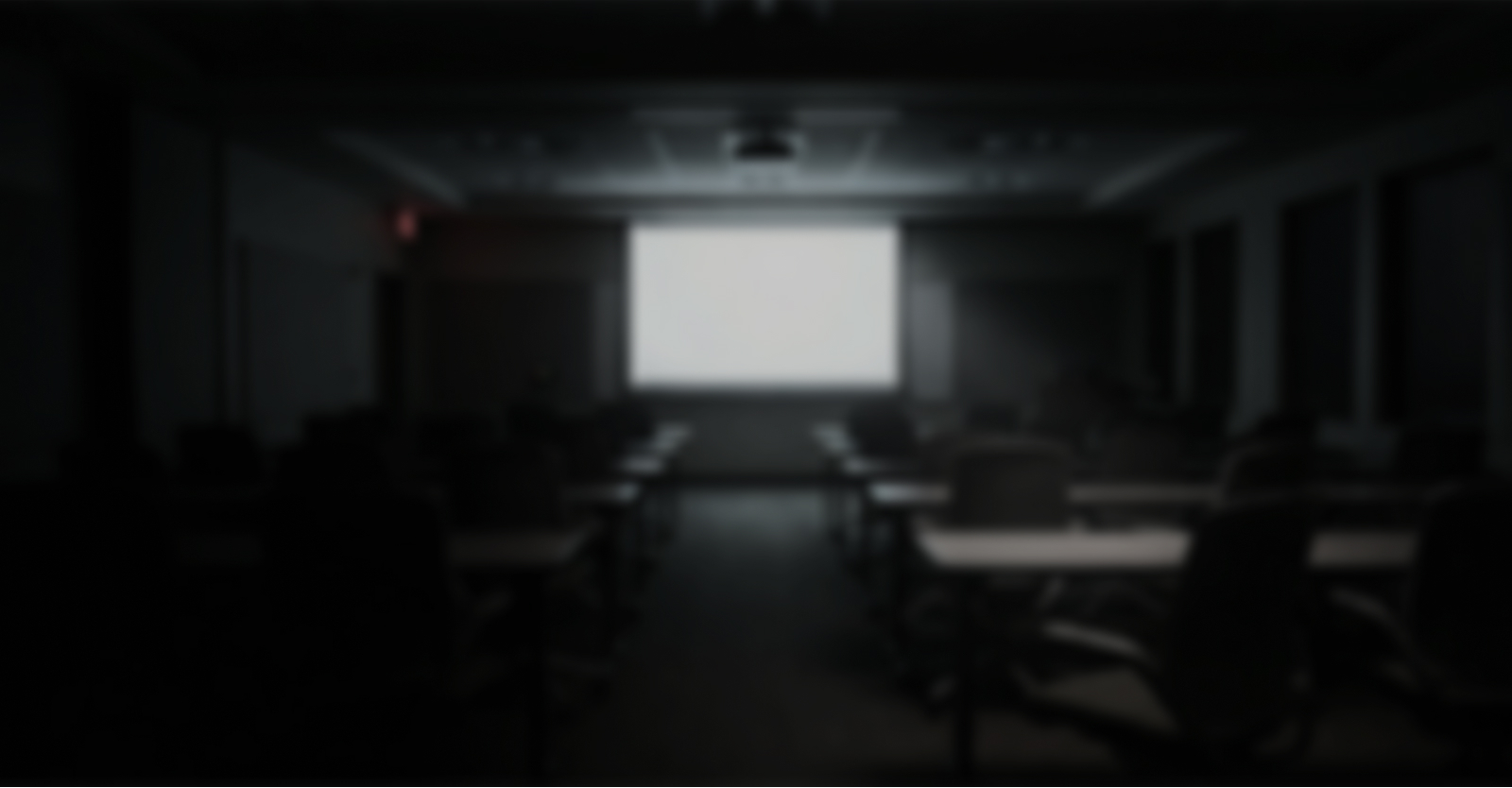 A dim, empty training room with rows of chairs facing a blank projection screen.